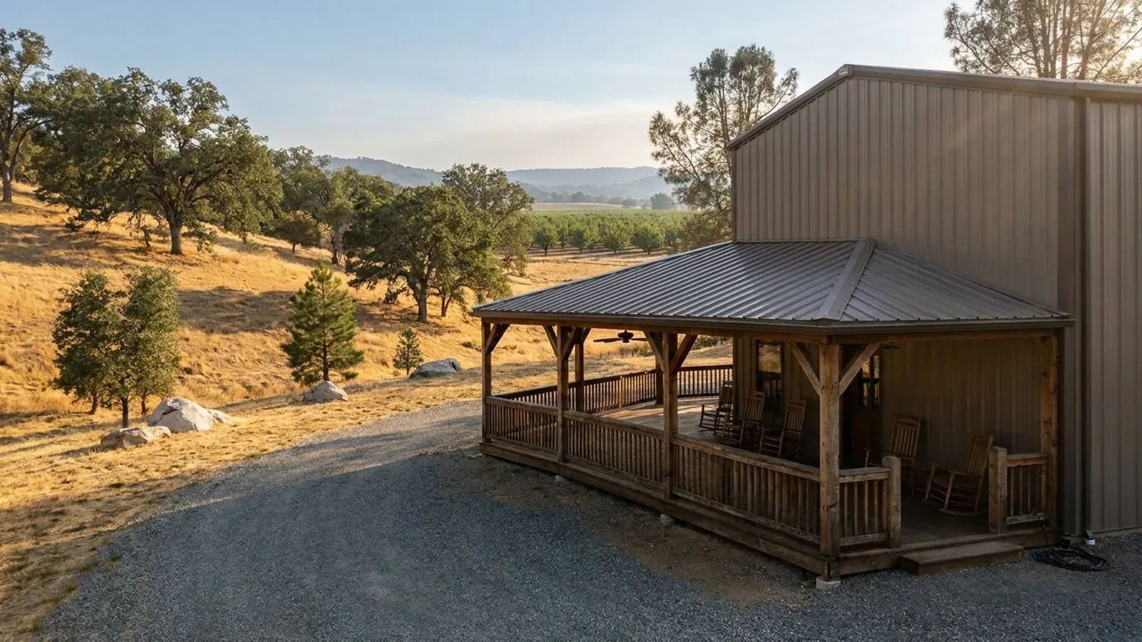 A barndominium exterior showing a deep wrap-around covered porch with posts and railing along two sides of the building.