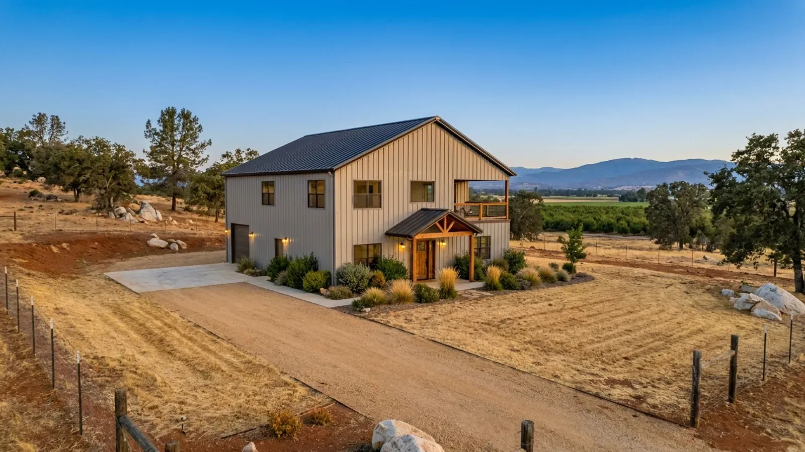 A completed two-story barndominium with visible second-story windows and a small covered balcony above the entry porch.